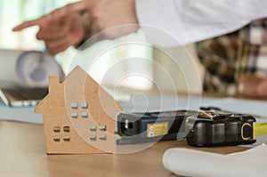 Wooden house model and tools on workplace desk with construction worker team working for start up plan new project contract in off