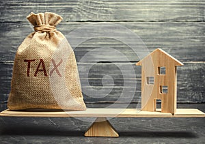 Wooden house and a money bag with the word Tax on the scales. Taxes on real estate, payment. Register of taxpayers for property.