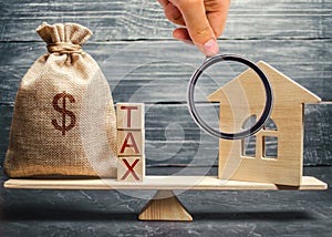 Wooden house and a money bag with the word Tax on the scales. Taxes on real estate, payment. Register of taxpayers for property.