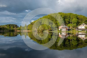 Wooden house near lake, forest reflected on water