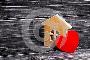 Wooden house with a red heart on a dark wooden background. A house for lovers, a honeymoon. Purchase your own affordable housing