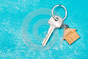 Wooden house shaped keychain and key on blue wooden background. Free space