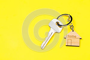 Wooden house shaped keychain and key on yellow background. Free space