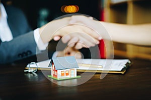 Wooden house on the table background with real estate agents and customer shaking hands after signing contract for realty purchase photo