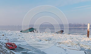 Wooden house and two boats trapped on the frozen river