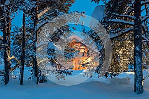 Wooden house with warm light in dark cold winter forest