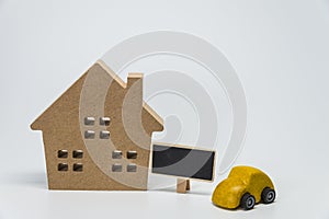 Wooden house, yellow car toy and small black board with white background and selective focus