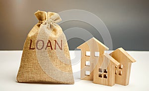 Wooden houses and a bag with the word Loan. Buying a home in debt. Family investment in real estate and risk management concept.