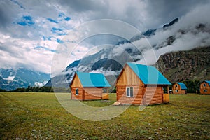 Wooden houses in a green valley on a background of mountains in the fog and cloudy sky, close-up. Tourist base in the Altai