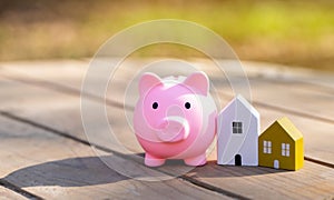 Wooden houses and piggy bank stands outdoors on a sunny day. Real estate and investments in housing concept.