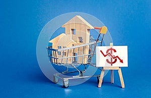 Wooden houses in a shopping cart and an easel with a red dollar arrow down chart. Fall of real estate market. Cheap rent. Reduced