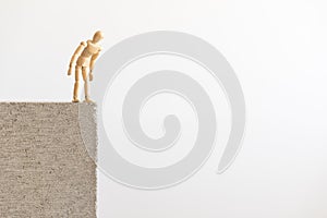 Wooden human figure standing on the edge of a concrete block, looking down