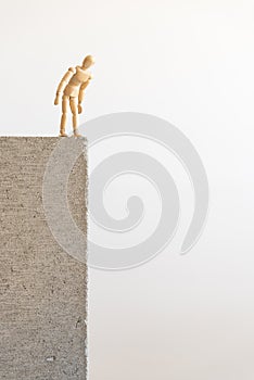 Wooden human figure standing on the edge of a concrete block, looking down