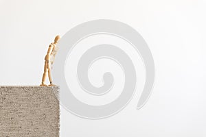 Wooden human figure standing on the edge of a concrete block, looking down