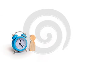 Wooden human figure stands near a blue alarm clock on a white ba