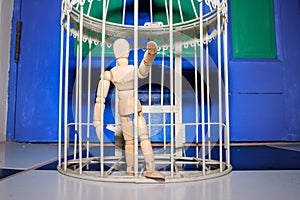 Wooden Human Manikin locked inside a white ornamental bird cage