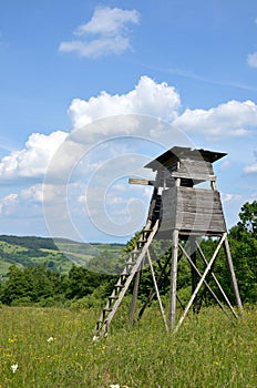 Wooden hunting tower on green meadow in sunshine