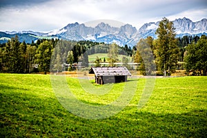 Wooden hut on green meadow against Alps mountains near Schwarzsee lake on sunny beautiful summer day near Kitzbuhel