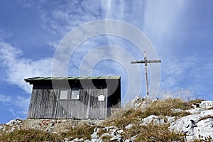 Wooden hut and summit cross Benediktenwand mountain at sunset in Bavaria, Germany