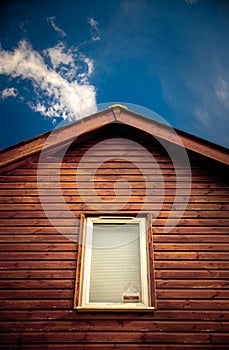 Wooden hut with window and roof against blue sky and clouds