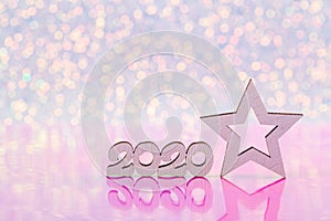Wooden icon with 2020 digits and white New Year star on white glitter sparkling and pink background with bokeh