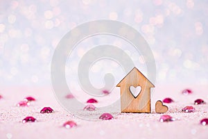 Wooden icon of house with hole in form of heart on glitter shiny light pink background with jems and bokeh lights photo