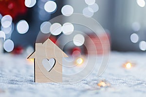 Wooden icon of house with hole in form of heart with red home Christmas decor and blurred bokeh background in daylight