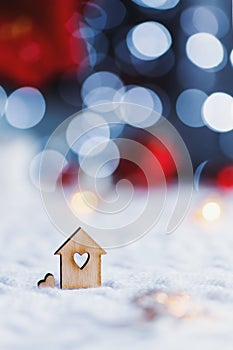 Wooden icon of house with hole in form of heart with red home Christmas decor and blurred bokeh background in daylight