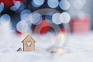 Wooden icon of house with hole in form of heart with red home Christmas decor and blurred bokeh background in daylight