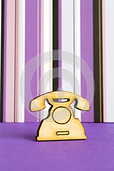 Wooden icon of telephone on purple striped background
