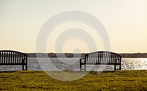 Wooden isolated benches on the waterfront overlooking a calm river at sunset
