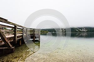 Wooden jetty in the beautiful Lake Bohinj in the Triglav National Park in Slovenia on misty morning in autumn