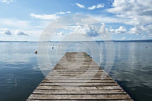 Wooden jetty for boats against a blue sky with some clouds. Floating buoys. Hills on background. Bolsena lake, Italy