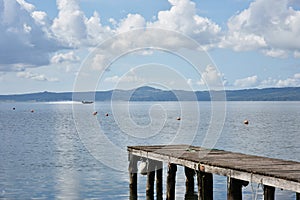 Wooden jetty for boats against a blue sky with some clouds. Floating buoys. Hills on background. Bolsena lake, Italy