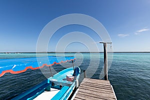 wooden jetty for boats on a blue and blue crystalline Caribbean sea with a moored blue boat . Caribbean fishing boat with a