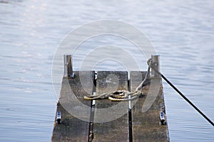 wooden jetty for boats and an old rope in the blue water background with copy space, selected focus, narrow depth of field