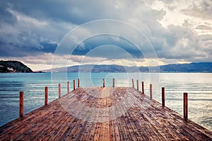 Wooden jetty on the calm sea, mountains and cloudy sky at dawn