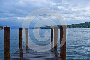 wooden jetty at a lake with ferry in the background in a cloudy day