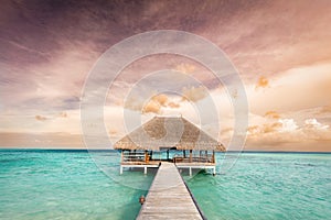 Wooden jetty leading to relaxation lodge. Maldives islands at sunrise