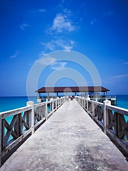 Wooden jetty in the noon under clear blue skies with people walking.