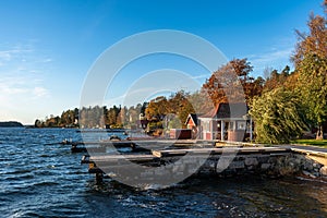 Wooden jetty pier on old stones base. Cabins small holiday cottages red houses on the shore. Beautiful autumn view of rocky and