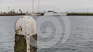 Wooden jetty pole with metal on a pier on a lake with calm waters and a boat in the background