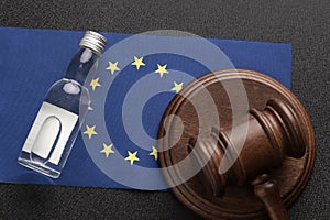 Wooden judge gavel and bottle of alcohol, EU flag background. Alcohol lawsuit in European Union concept