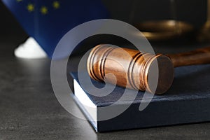 Wooden judge`s gavel and book on table against European Union flag, closeup. Space for text