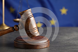 Wooden judge`s gavel and Scales of justice on grey table against European Union flag, closeup. Space for text