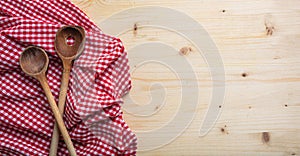 Wooden kitchen utensils on red checkered picnic tablecloth on wooden table, top view, copy space