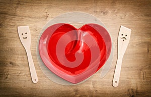 Wooden kitchen utensils and red heart plate. Funny tools