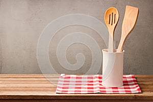 Wooden kitchen utensils on table with tablecloth over grunge wall background with copy space for product montage