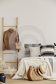 Wooden ladder with sweater and bag next to bed with striped bedding