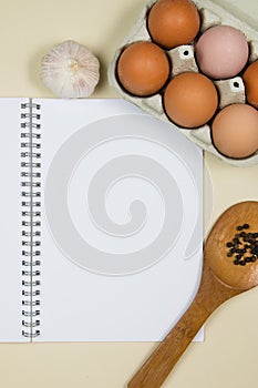 Wooden ladle with spices, eggs and garlic with a blank notebook page